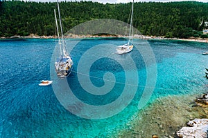 Crystal clear transparent blue turquoise teal mediterranean sea water of Foki Fiskardo Beach with some white yacht in