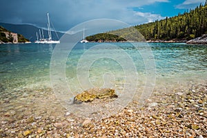 Crystal clear transparent blue turquoise teal mediterranean sea water of Foki Fiskardo Beach with some white yacht in