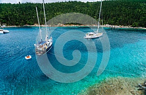 Crystal clear transparent blue turquoise teal mediterranean sea water of Foki Fiskardo Beach with some white yacht in