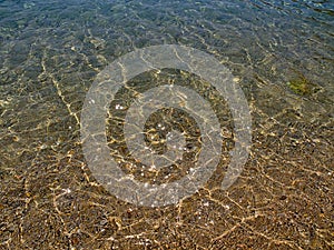 Crystal clear water close up in sandy beach, sunlight reflecting