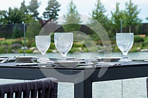 Crystal empty glasses, white plates and cutlery on a table in a beach restaurant. Table setting for a festive dinner