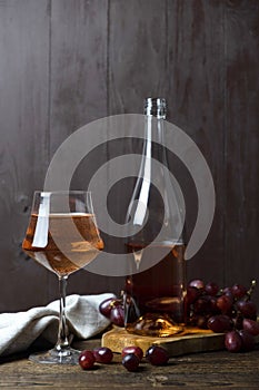 A crystal glass full of rose wine, next to a bottle and a bunch of red ripe fresh grapes. Vertical orientation. Place for text