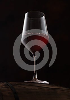 Crystal glass of red wine on top of wooden barrel on black