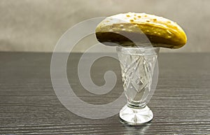 A crystal glass with vodka and a pickled cucumber placed.