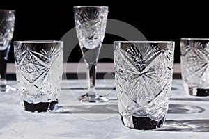 Crystal glasses on textured table with hard light and long clear shadow. Sun glare, light refraction on transparent faceted dishes