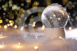 Crystal globe and Christmas lights on snow against blurred background, space for text.