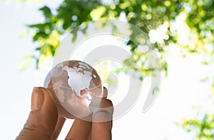 Crystal globe in the hand of a man against a background of blue sky and green foliage. Earth protection concept