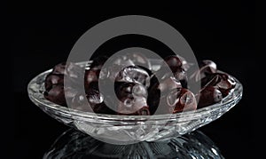 Crystal saucer with a bunch of dried dates on a dark mirror