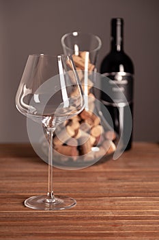 Crystal shiny glass, bottle of red wine, transparent decanter filled with corks on wooden table. Closeup, vertical, selective