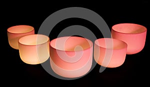 Crystal singing bowls with pink light on a dark background