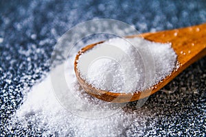 Crystals of shallow salt in a scoop, spoon on a dark gray table. Background for advertising salt. Table salty. Salted food.