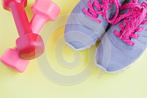 Csport grey sneakers with bright pink laes and pink dumbbells on light yellow background, healthy lifestyle, space for text