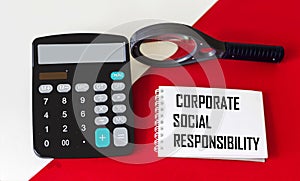 CSR corporate social responsibility concept on a notepad with a calculator and a magnifying glass on a red and white background