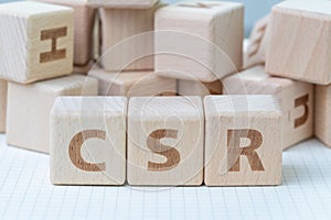 CSR, Corporate Social Responsibility concept, wooden cube block with letters forming acronym CSR on white gridline notebook,