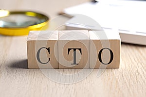 CTO on wooden cubes with magnifier and calculator, financial concept background