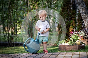 Cuate adorable caucasian blond little toddler boy in watering flowerbed flower pot with green plastic can outdoors. Fun baby boy