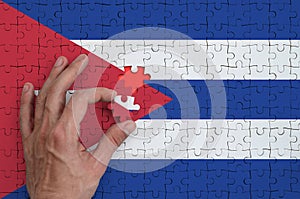 Cuba flag is depicted on a puzzle, which the man`s hand completes to fold