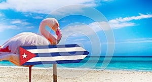 Cuba flag on wooden table sign on beach background with pink flamingo. There is beach and clear water of sea and blue sky in the