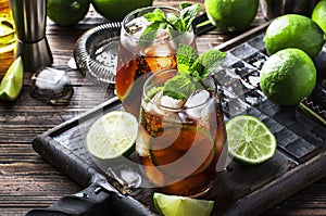 Cuba libre alcohol cocktail with golden rum, lemon juice, cola, lime and ice, dark bar counter background, bar tools, place for