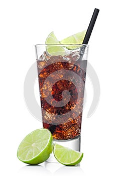Cuba Libre Cocktail in luxury tall glass with ice cubes and slices of lime with black straw on white with raw limes