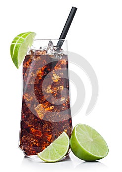 Cuba Libre Cocktail in luxury tall glass with ice cubes and slices of lime with black straw on white with raw limes
