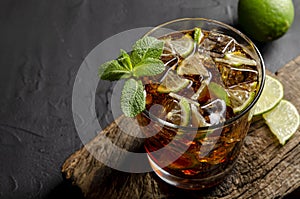 Cuba libre, rum and cola cocktail in glass with a lime and mint on black background