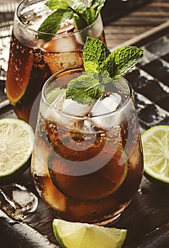 Cuba libre or rum cola cocktail with strong alcohol, lemon juice, lime and ice, dark background, steel bar tools, copy space