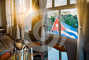 A Cuban flag wave on the exterior of a house during the afternoon, some sun rays going through.