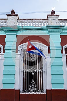 Cuban flag waving in the wind on the facade of a mint green colonial house in Camaguey, Cuba