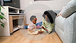 Cuban mother playing with a ball with her toddler daughter on the floor.