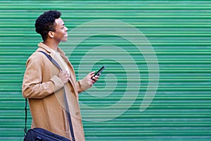 Cuban young man looking forward using his smartphone near green blinds.