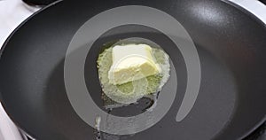 Cube of butter that begins to melt slowly in a pan on a gas stove