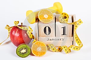 Cube calendar with date of 1 January, fruits, dumbbells and tape measure, new years resolutions concept