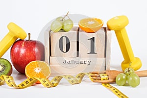 Cube calendar with date of 1 January, fruits, dumbbells and tape measure, new years resolutions concept