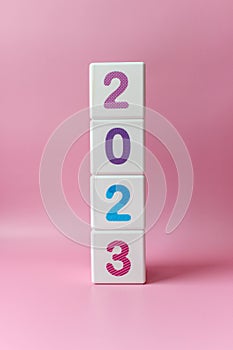 Cube tower with colorful numbers 2023 in center of the photo on pink background. New year, calendar.