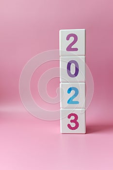 Cube tower with colorful numbers 2023 on pink background with copy space. New year, calendar.