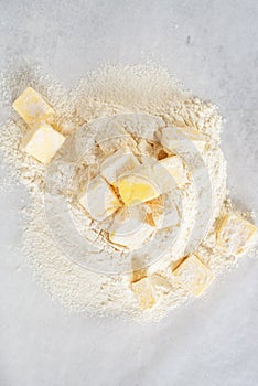 cubes cold butter on all-purpose flour with a jar of ice water in preparation to make puff pastry.