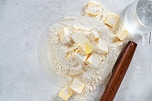 Cubes cold butter on all-purpose flour with a jar of ice water in preparation to make puff pastry.