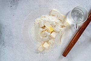 Cubes cold butter on all-purpose flour with a jar of ice water in preparation to make puff pastry.