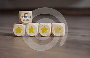 Cubes, dice or blocks with german words for Please rate us - Bitte bewerten Sie uns - and with yellow stars on wooden background