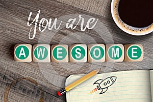 Cubes, dice or blocks with message you are awesome on wooden background with pencil, coffee, sketch book