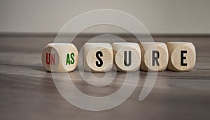 Cubes, dice or blocks with unsure and assure on wooden background