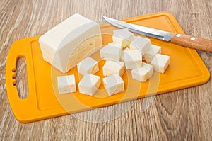 Cubes of feta cheese on plastic cutting board, kitchen knife