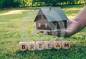 Cubes form the abbreviation BREEAM Building Research Establishment Environmental Assessment Method in front of a model house photo