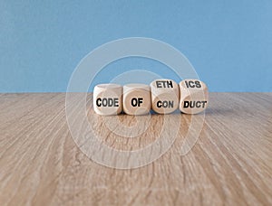 Cubes form the expression \'code of conduct\' and \'code of ethics\'. Beautiful blue background, wooden table.