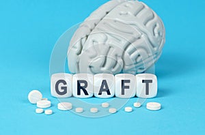 Cubes lie on the table among the pills and imitation of the brain. The text on the dice - GRAFT