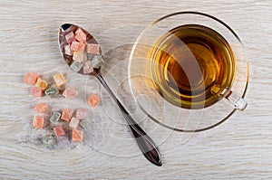 Multicolor rakhat-lukum in spoon, scattered rakhat-lukum, cup of tea on saucer on table. Top view photo