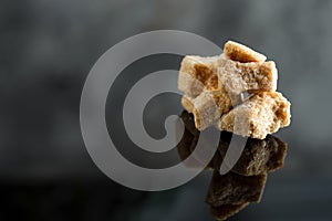 Cubes of natural cane brown sugar on a black background with reflection.