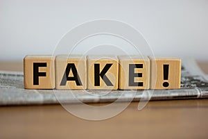 Cubes placed on a newspaper form the word `fake`. Beautiful wooden table. White background. Business concept. Copy space