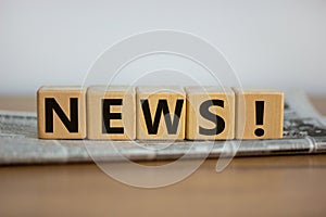 Cubes placed on a newspaper form the word `news`. Beautiful wooden table. White background. Business concept. Copy space